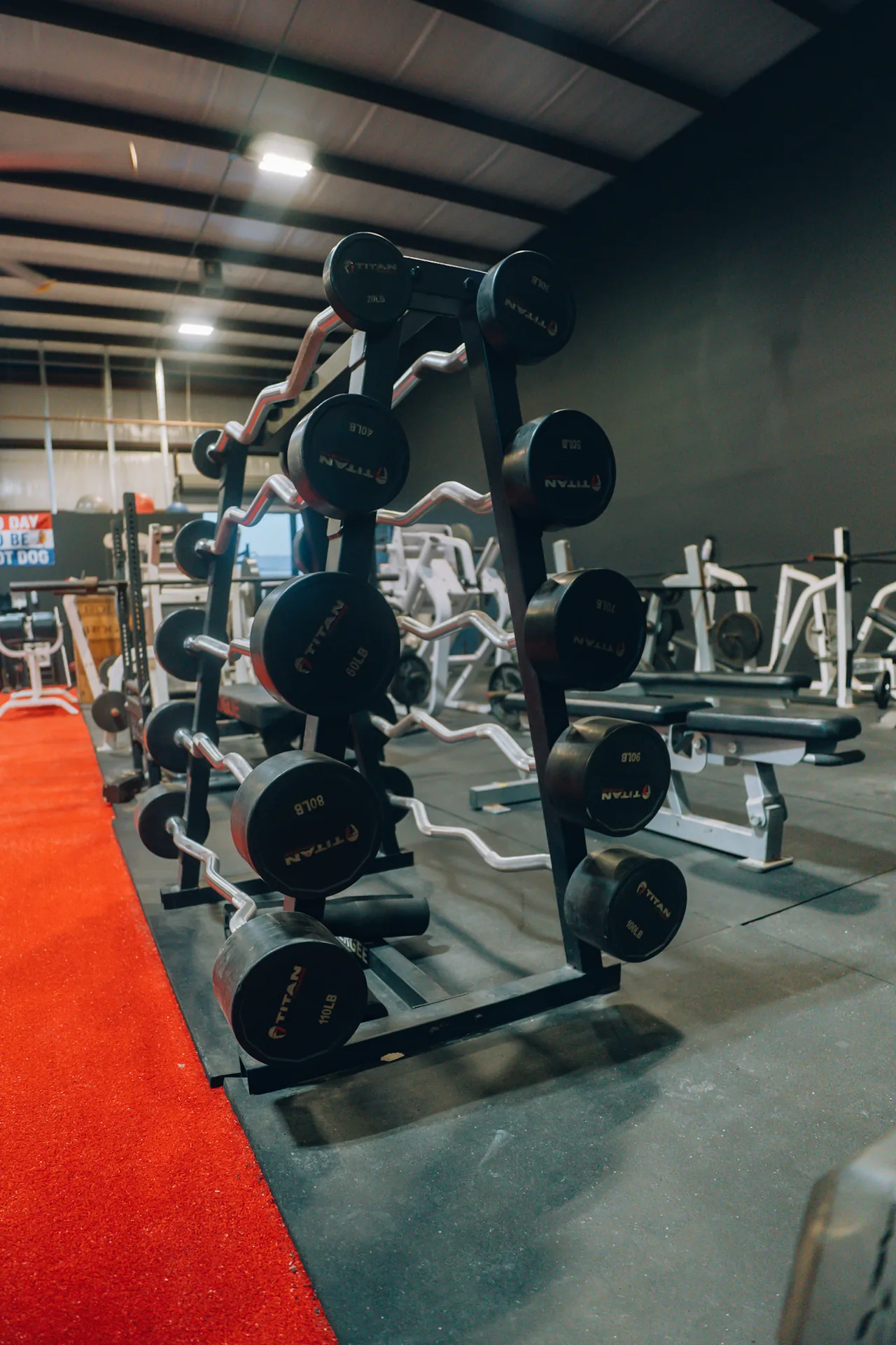 Fixed-weight barbells beside the red turf at Redline Barbell